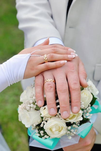 Mani con fedi nuziali e bouquet da sposa