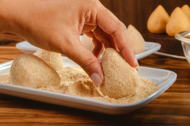 ブラジルのコロッケをパン粉をまぶす女性の手-クローズアップ