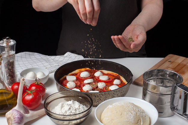 Hands of the woman cook sprinkle Italian raw pizza.