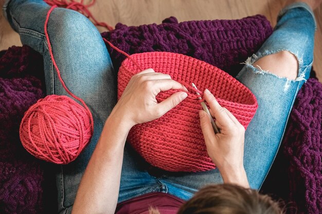 Hands woman in a cozy home setting knits from a pink thread. Top view. Copy, empty space for text.