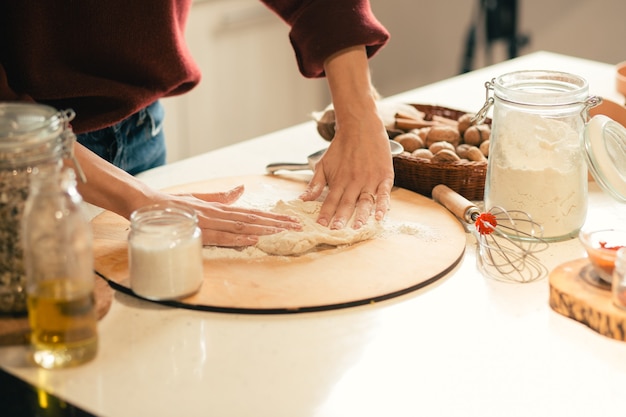 Hands of woman on the dough. Wicker basket and a jar of flour by her side