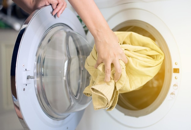 Hands woman getting in dirty clothes into washing machine doing\
laundry at house
