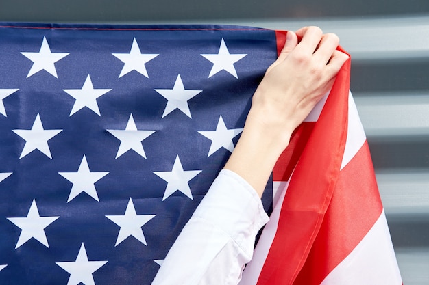 Руки женщины, висит флаг США на серой стене, концепция день независимости США