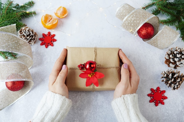 Hands of woman holding Christmas gift box with winter decorations