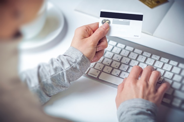 Hands of a woman holding a credit card and using a computer for online purchases