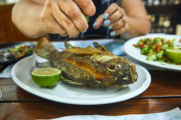 Photo hands of a woman holding a lemon and pouring fried fish on a plate slave restaurant.