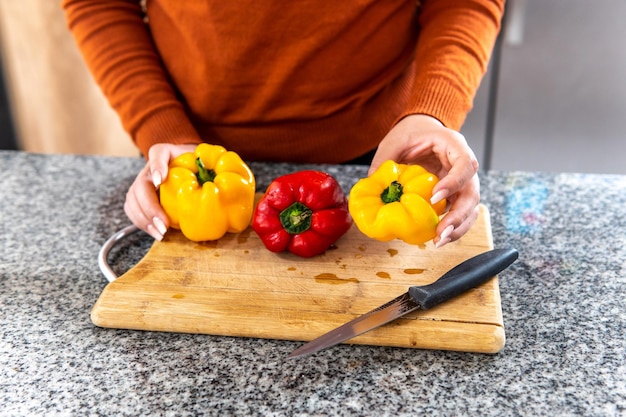 hands of a woman preparing yellow and red peppers on a cutting board