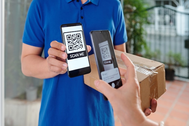 Hands of woman scanning QR code on smartphone of courier and paying for parcel delivery