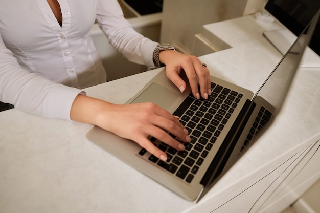 Hands of a woman in a white shirt working behind a laptop