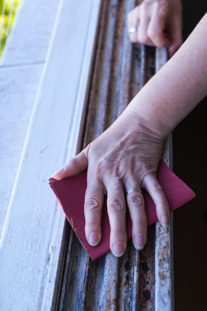 Hands of a woman with a sandpaper sanding a window frame before painting Empowered woman concept Vertical Orientation