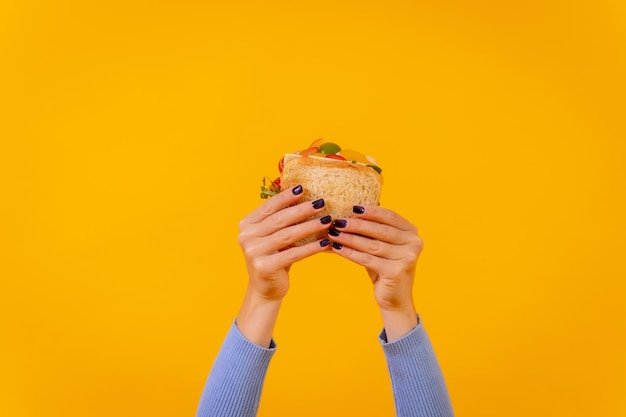 Hands of a woman with a sandwich on a yellow background healthy food