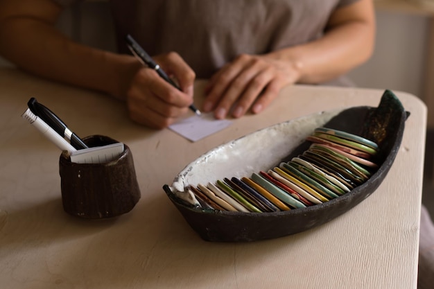 Hands of woman working in pottery workshop and choosing color for future product from palette