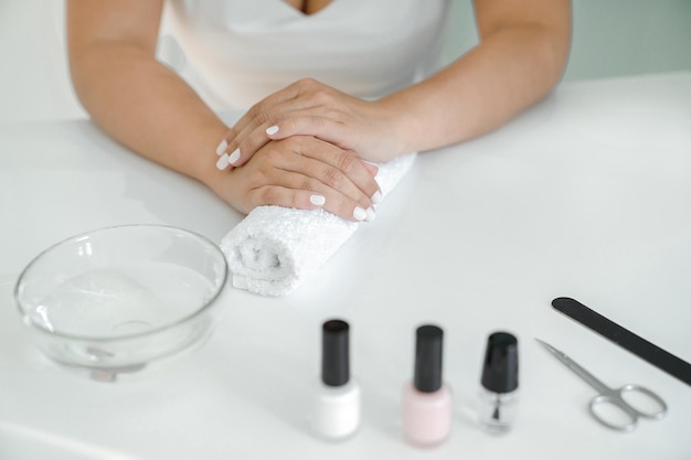 Hands of women with white manicure lie on towel roller, manicure accessories are lying next to it.