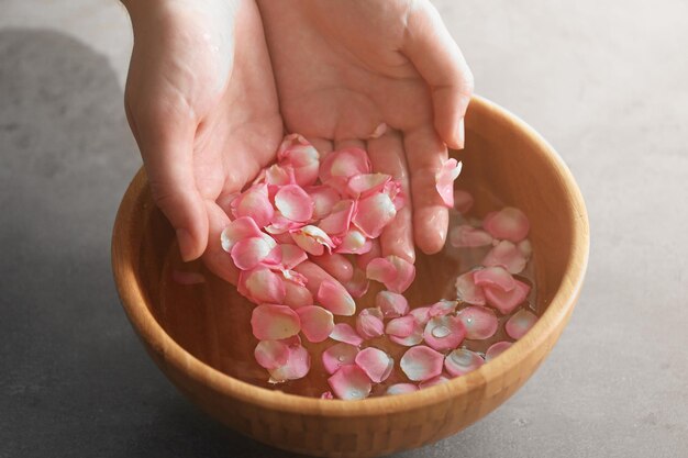 Hands in wooden bowl with petals and water