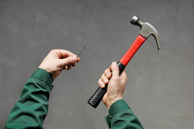 Hands in work clothes hold nail and hammer closeup on textured gray background