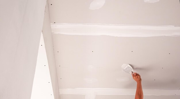 Foto mani di operaio intonaco soffitto putty bianco e trowel artigiano al lavoro intonacando un soffitto