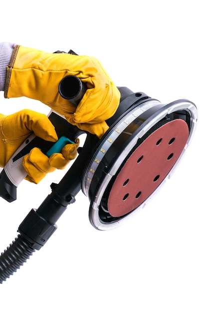 The hands of a worker in yellow protective gloves hold a vacuum electric wall grinder