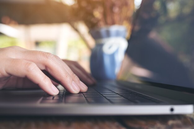 hands working and typing on laptop keyboard on wooden table in cafe 