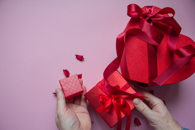 Le mani avvolgono il contenitore di regalo rosso a forma di cuore con il nastro rosso