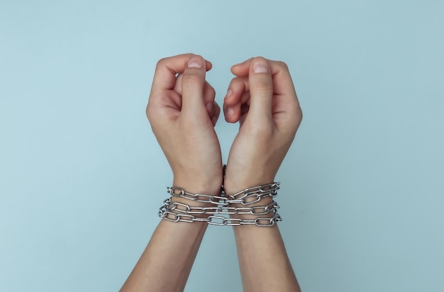 Hands wrapped in a steel chain on a blue background. forced
detention, imprisonment or arrest