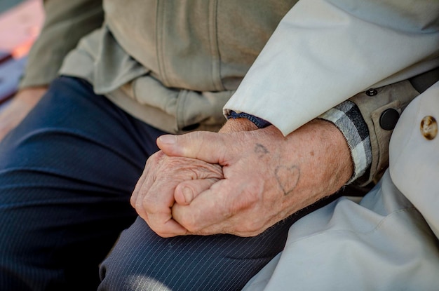 Hands in wrinkles of the old tattoo in the shape of heart Elderly couple holding hands outdoors