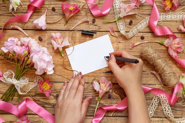 Фото Руки пишут открытку на деревянном столе между розовыми цветами, вид сверху