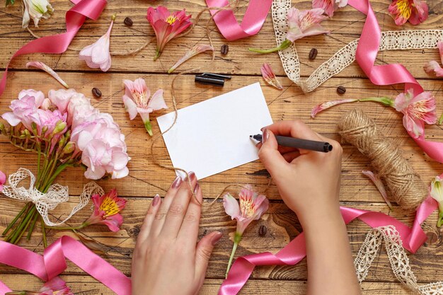 Hands Writing a card on a wooden table between pink flowers top view