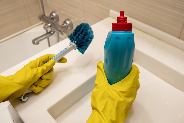 Photo hands in yellow gloves hold cleaning agent and blue sponge on the handle for cleaning the bathroom. the concept of homework, disinfection