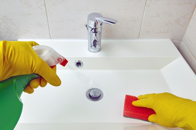 Hands in yellow protective gloves spray disinfectant to clean sanitary equipment in the bathroom