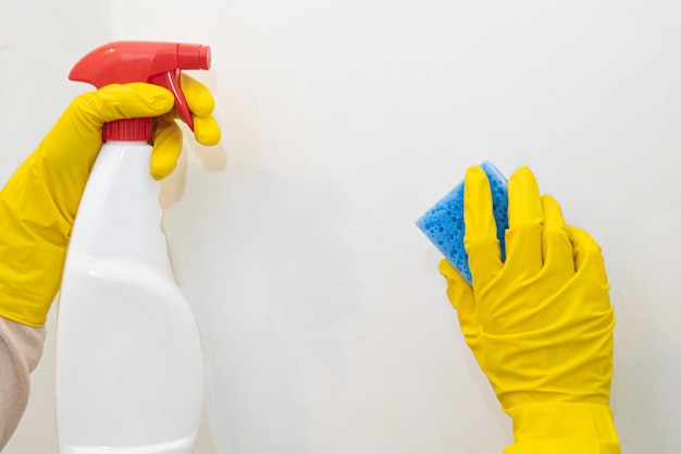 Hands in yellow rubber gloves washing the tiles in the bathroom.