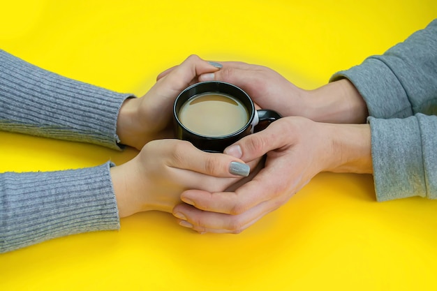 Hands on a yellow surface with black cup with coffee