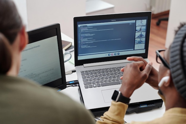 Mani di giovane uomo di colore sulla tastiera del laptop con chat video sullo schermo