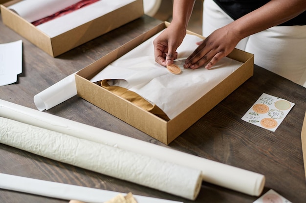 Hands of young black woman putting sticker on top of wrapping paper