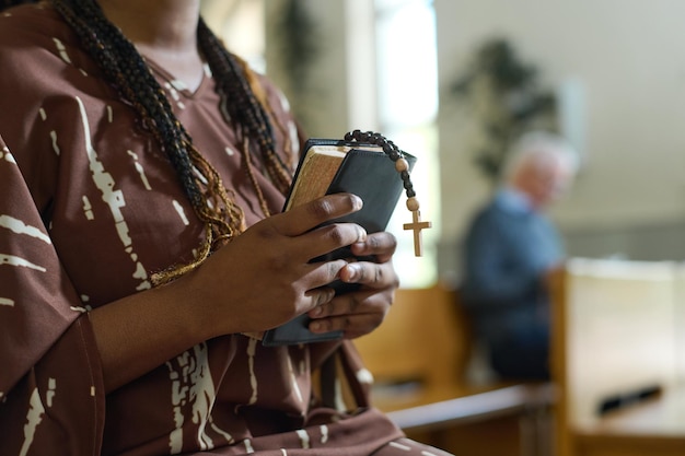 Hands of young black woman with holy bible and rosary beads\
with cross