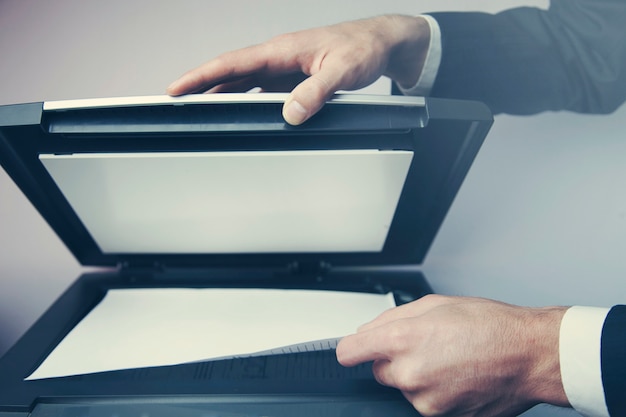The hands of a young businessman is placing a document on a flatbed scanner