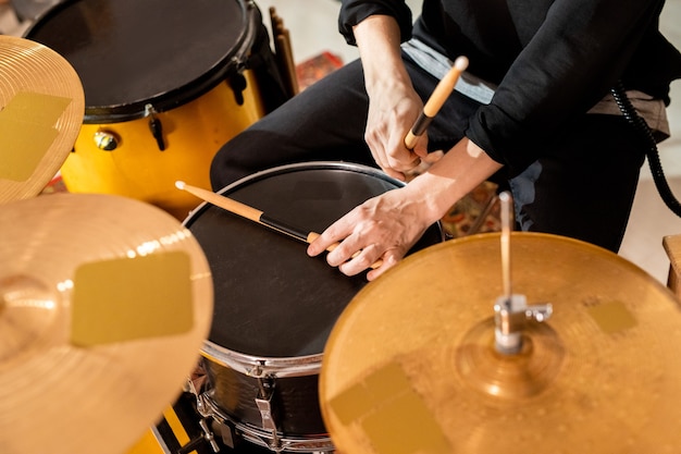 Hands of young casual drummer taking drumsticks from top of black drum while sitting by drumset and going to start individual rehearsal