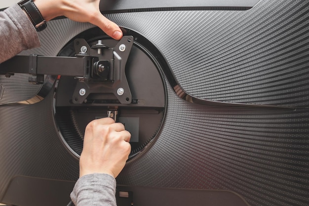 Hands of a young caucasian guy manually twists a nut on a bracket while installing on a computer monitor