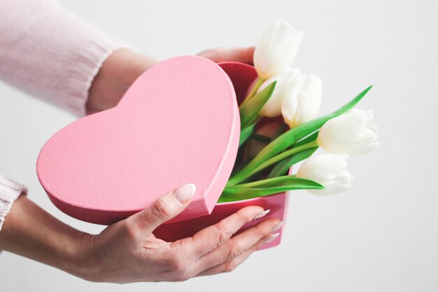 The hands of a young caucasian woman with a beautiful and delicate manicure hold a pink heart box