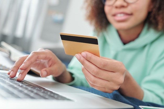 何かを購入しようとしている間オンラインショップで商品をスクロールするラップトップのキーパッド上のクレジットカードを持つ若い現代女性の手