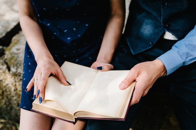 Una giovane coppia di mani seduta legge un libro aperto sulle ginocchia