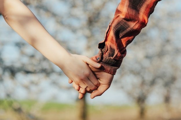 Руки молодой пары в весеннем цветущем саду на помолвке. Кольцо на пальце девушки.