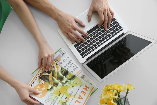 Photo hands of young couple with laptop and magazines at home