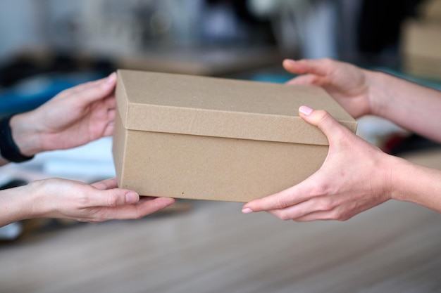 Hands of young craftswoman passing packed box with leatherwear to buyer