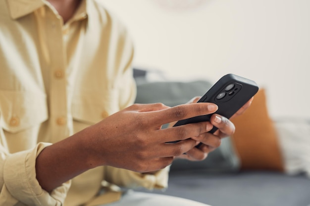 hands of young dark skinned woman with finger rings using online app on mobile phone making