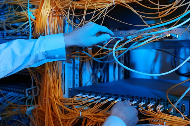 Hands of young engineer connecting cables in server room