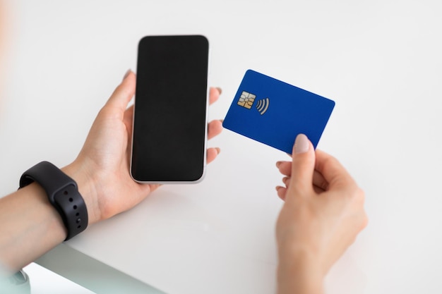 Hands of young european woman use smartphone with blank screen and credit card on white table