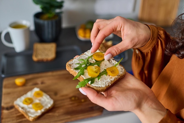 Hands of young female vegetarian putting chopped tomatoes on sandwich