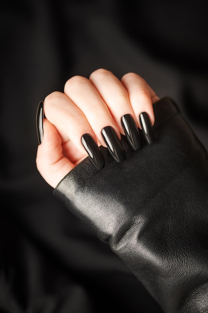 Photo hands of young girl with black manicure on nails on black background