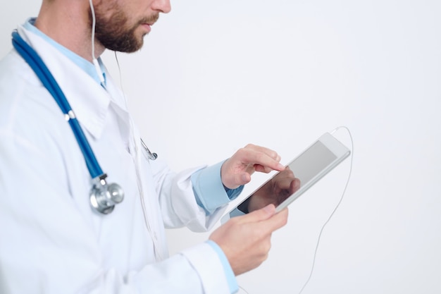 Hands of young male doctor in earphones pointing at tablet display while taking online patients and giving them medical recommendations