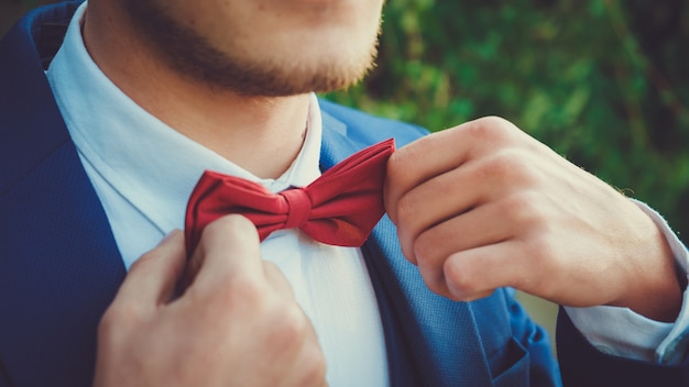 Hands of a young man in a blue suit with a red bow tie close up